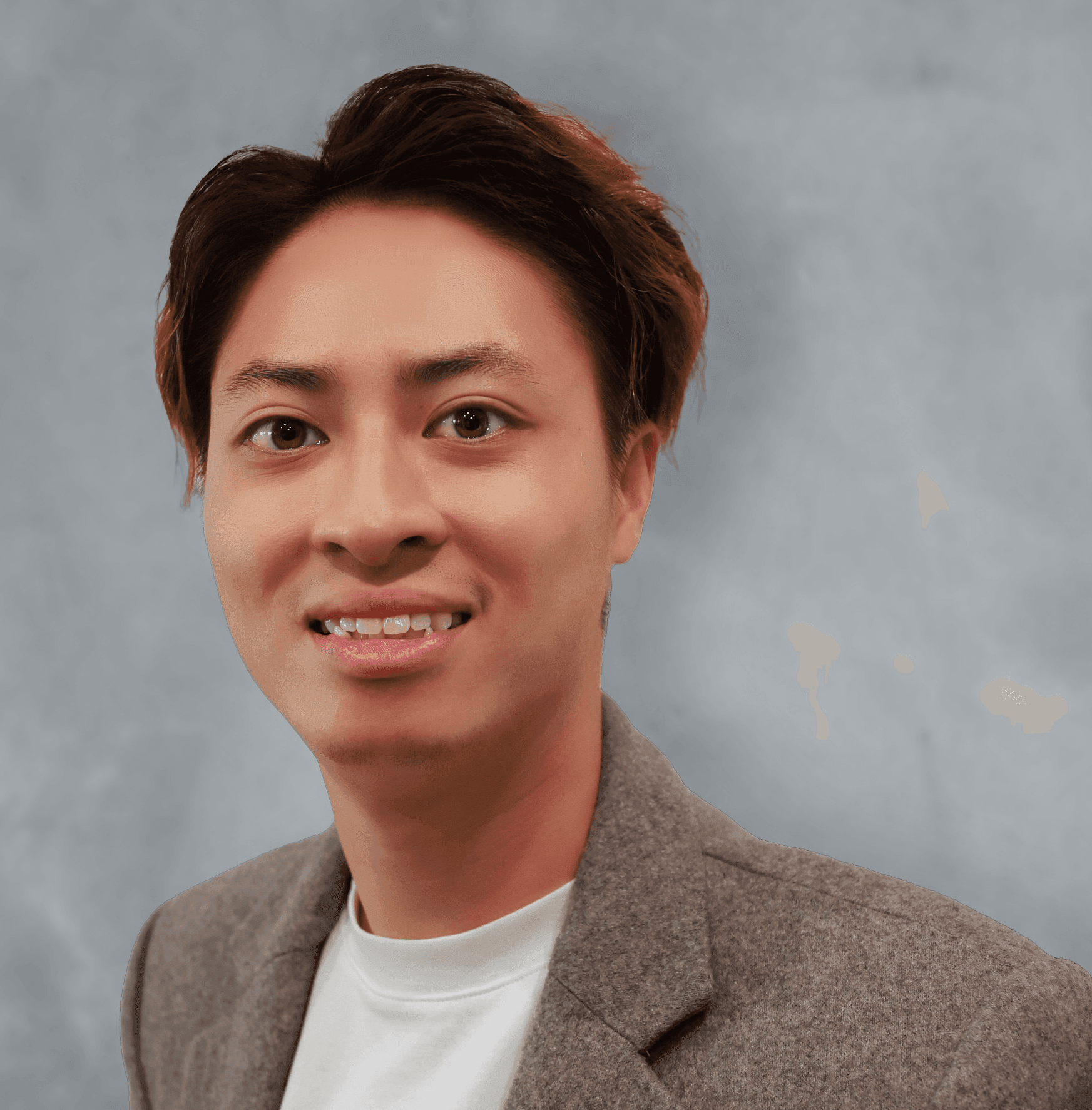 Portrait of a smiling person wearing a white shirt and a gray blazer with a neutral background.